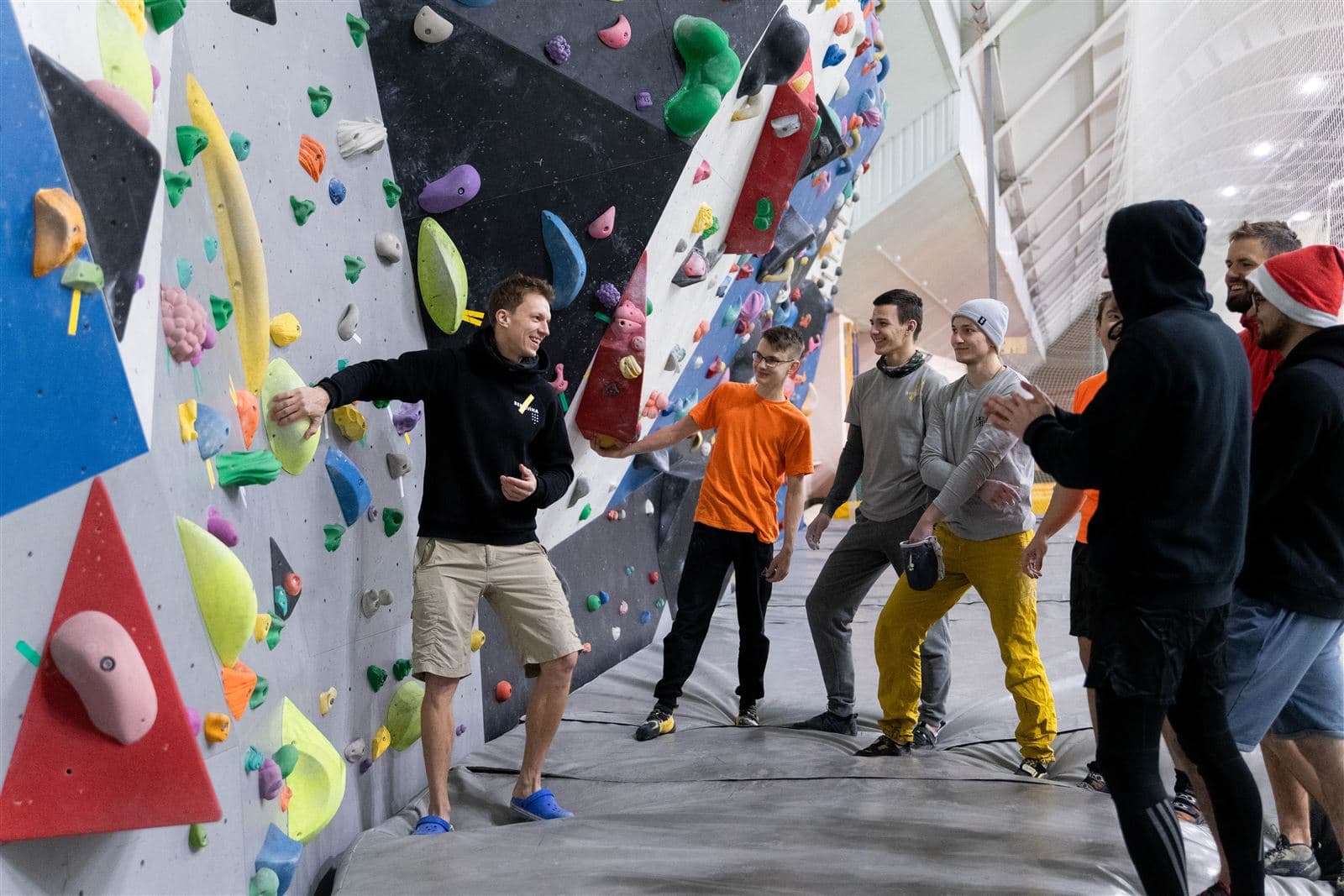 Alex Voit coaching a group of climbers at an indoor bouldering wall.